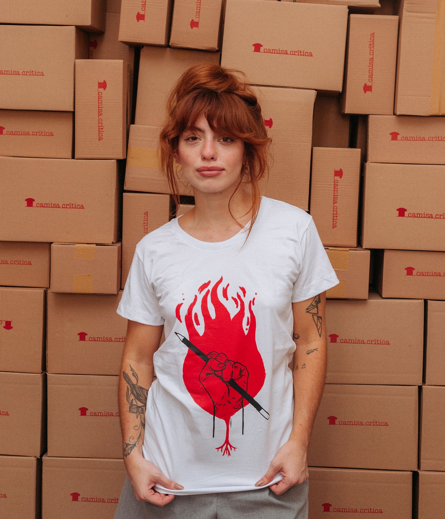 Mulher vestindo Camiseta Baby Look Estampa: Punho cerrado com um lápis na mão sobrepostos à uma raiz e um círculo de fogo.