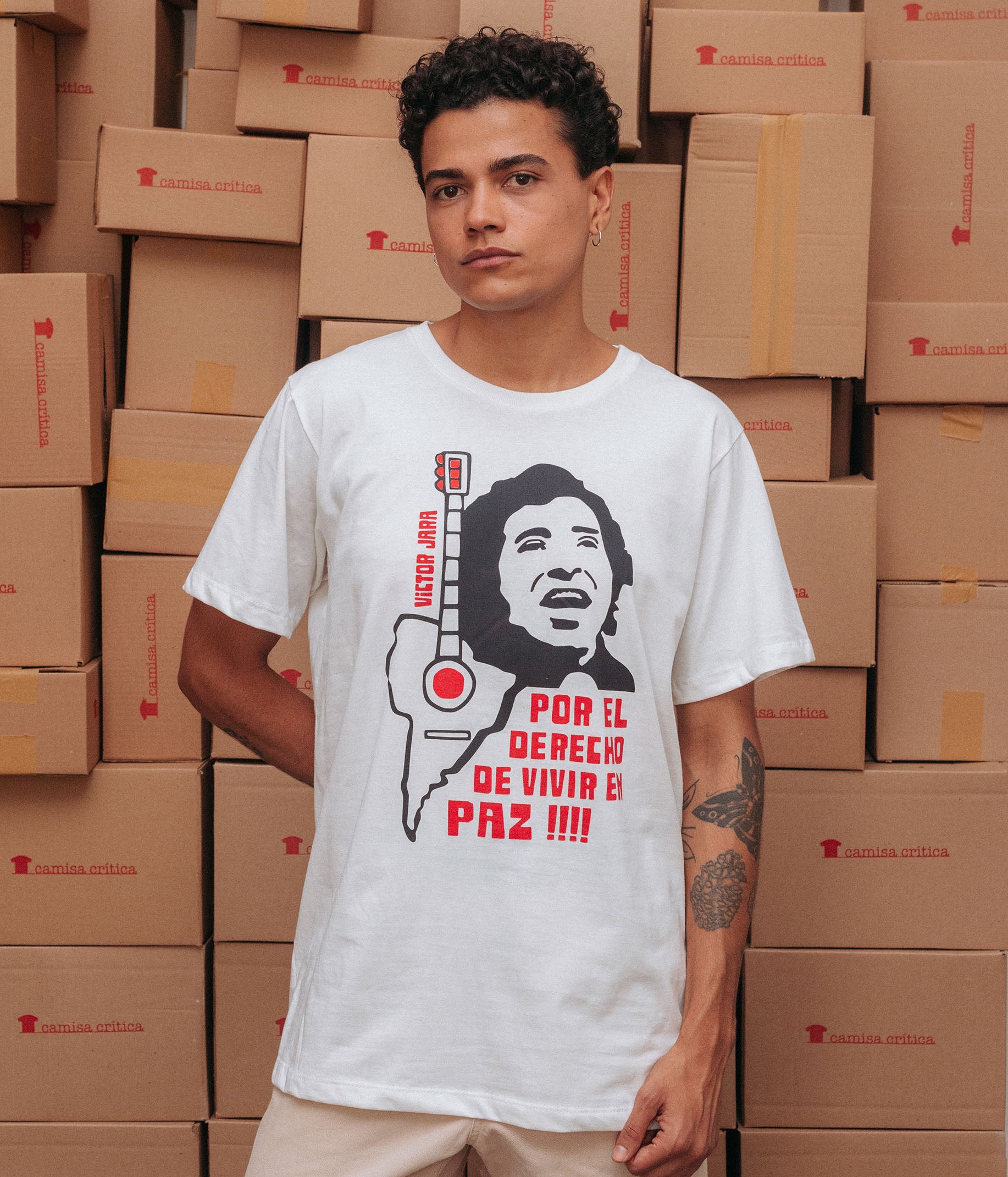 Homem vestindo Camiseta Básica Estampa: Ilustração composta de texto e imagens: texto “victor jara” à esquerda. Ainda na esquerda um violão com o tampo em formato da América do Sul. À direita encima o rosto de Victor Jara cantando e baixo dele o texto: por el derecho de vivir en paz!!!!