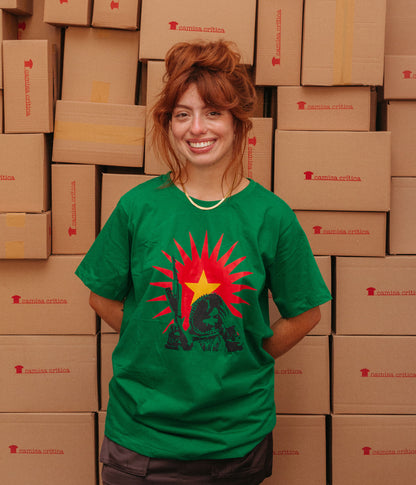 Mulher vestindo Camiseta Básica Estampa: uma guerrilheira kurda com arma em riste sobrepõem um sol que irradia com uma estrela no meio.