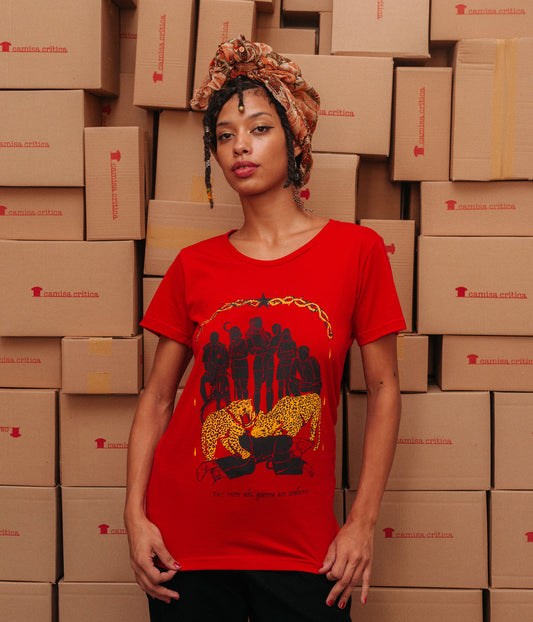 Mulher vestindo Camiseta Baby Look Estampa:Moldura superior com espinhos e uma estrela preta no meio. Seis personagens são apresentados num arco: o entregador de delivery com uma camiseta do PT, uma agricultora com uma foice, uma mulher de dreads com uma criança de colo, uma indígena de braços cruzados e um rapaz agachado sem camisa. Eles assistem duas onças atacarem um executivo com chapéu da ku klux klan. Detalhe pra cruz de ferro na sua meia. Abaixo está escrito: paz entre nós, guerra aos senhores.