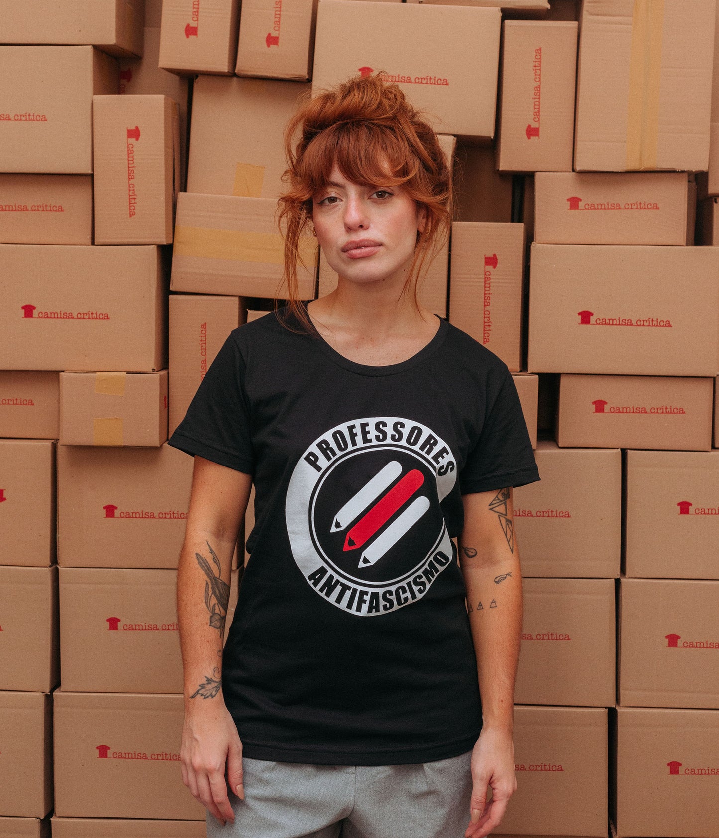 Mulher vestindo Camiseta Baby Look Estampa:  Três lápis paralelos na diagonal. Ao redor um círculos onde está escrito Professores Antifascismo.