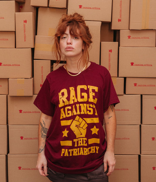 Mulher vestindo Camiseta Básica Estampa: texto Rage Against The Patriarchy com punho cerrado no meio com duas estrelas, uma de cada lado, e duas linhas paralelas