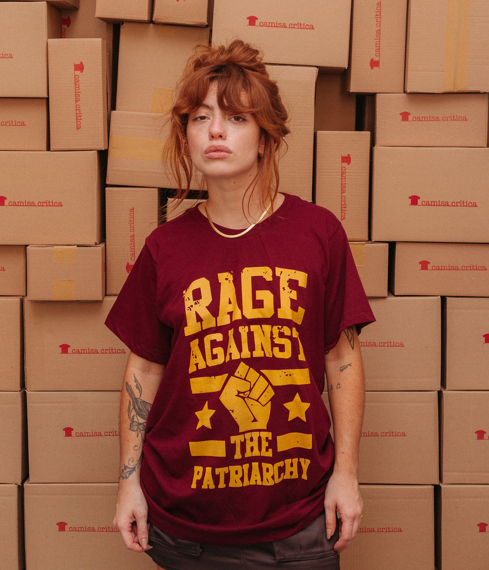 Mulher vestindo Camiseta Básica Estampa: texto Rage Against The Patriarchy com punho cerrado no meio com duas estrelas, uma de cada lado, e duas linhas paralelas