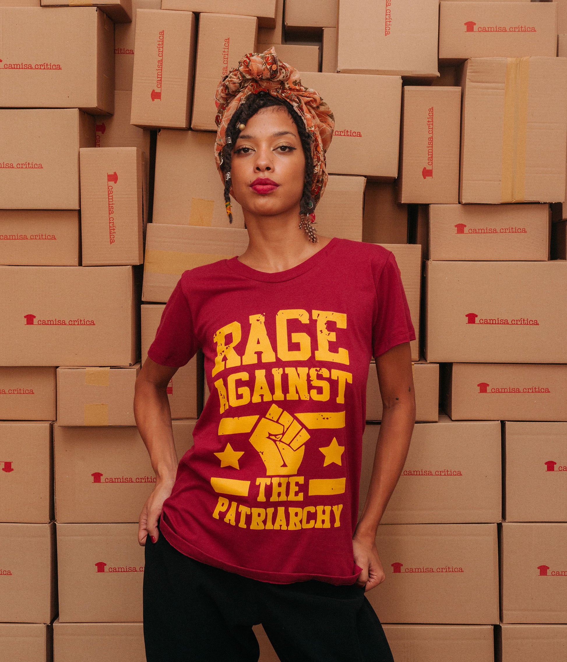 Mulher vestindo Camiseta Baby Look Estampa:  texto Rage Against The Patriarchy com punho cerrado no meio com duas estrelas, uma de cada lado, e duas linhas paralelas